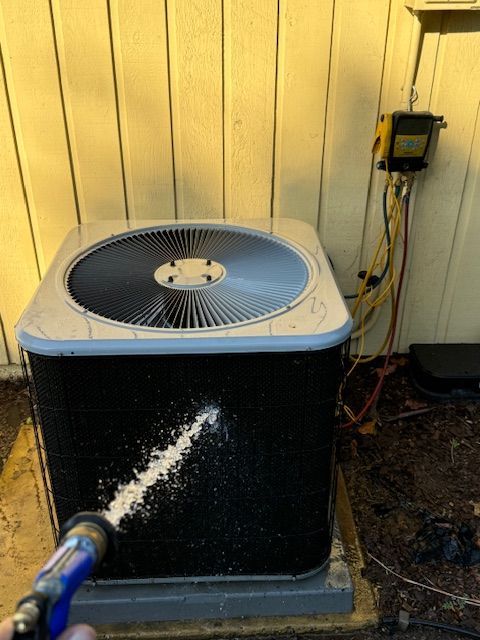 A person is cleaning an air conditioner with a hose