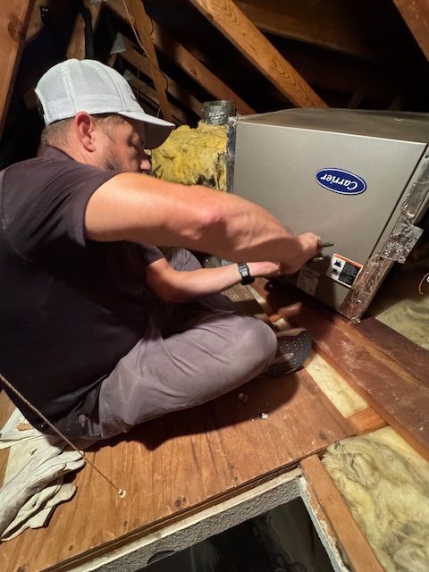 A man is sitting on the floor working on a carrier air conditioner.