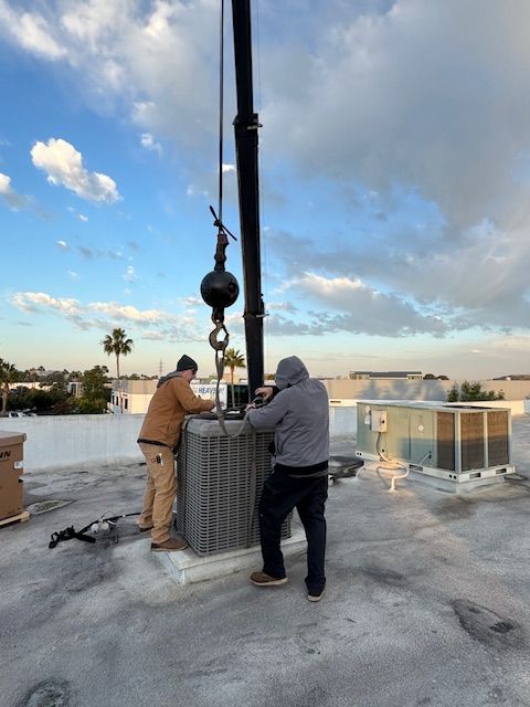 Two men are working on an air conditioner on a roof
