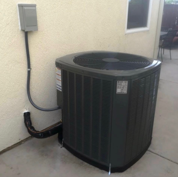 A gray air conditioner is attached to the side of a building
