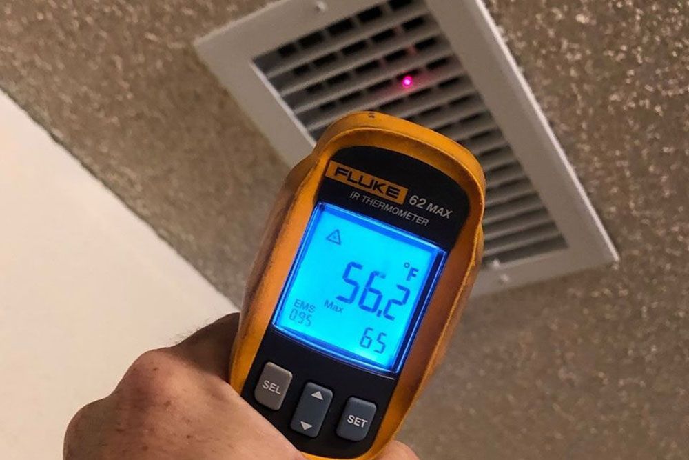 A person is holding a fluke thermometer in front of a vent.