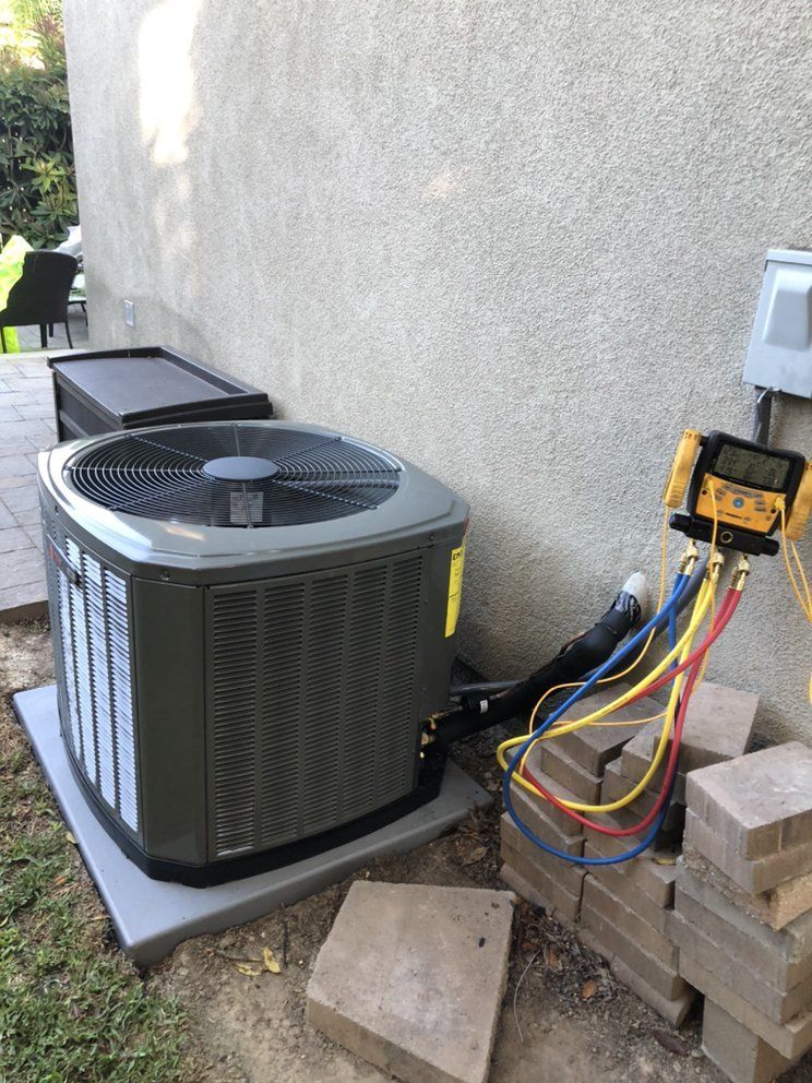 A gray air conditioner is sitting next to a wall next to a stack of bricks.