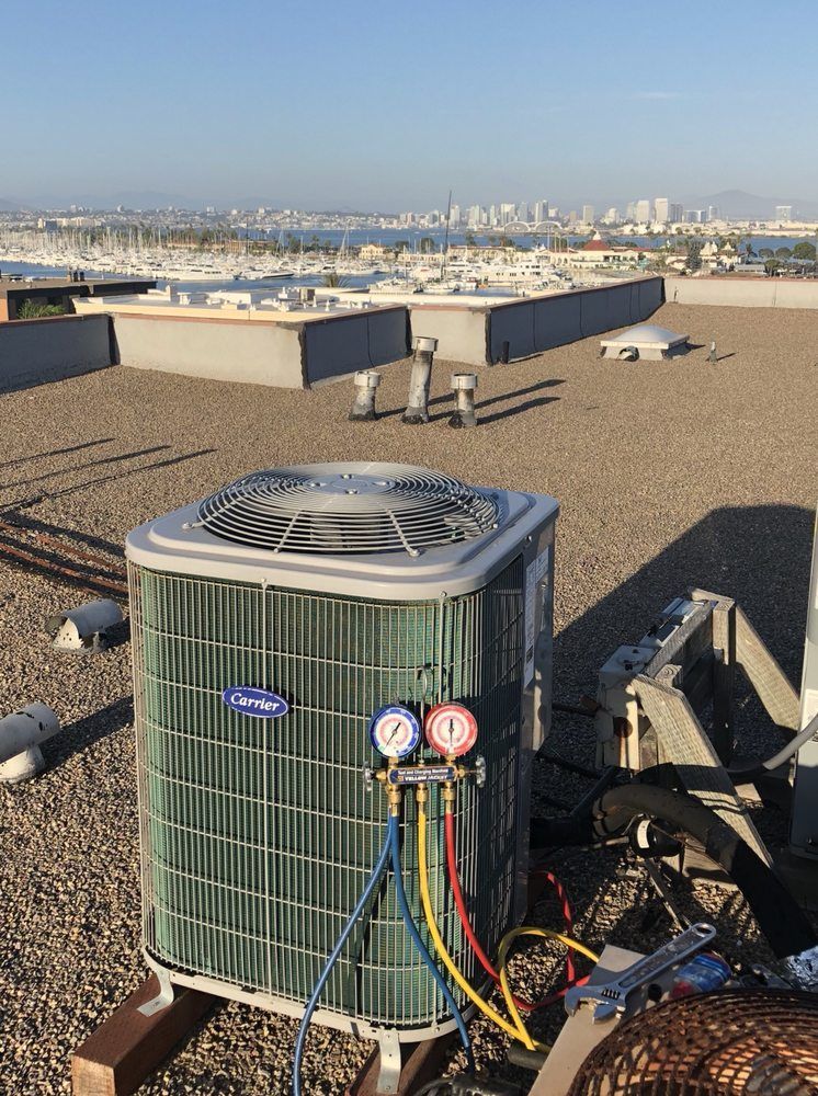 An air conditioner is sitting on top of a roof with a city in the background.
