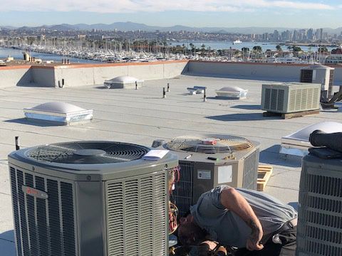 A man is working on an air conditioner on the roof of a building.