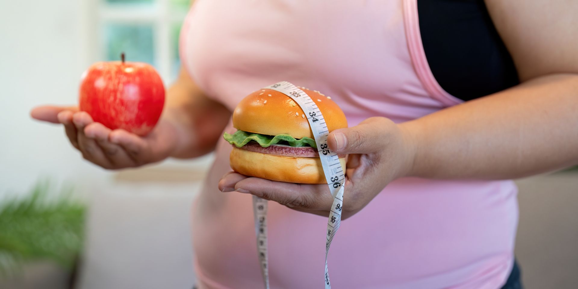 Person holding an apple in one hand and a dripping burger in the other, illustrating food contrast