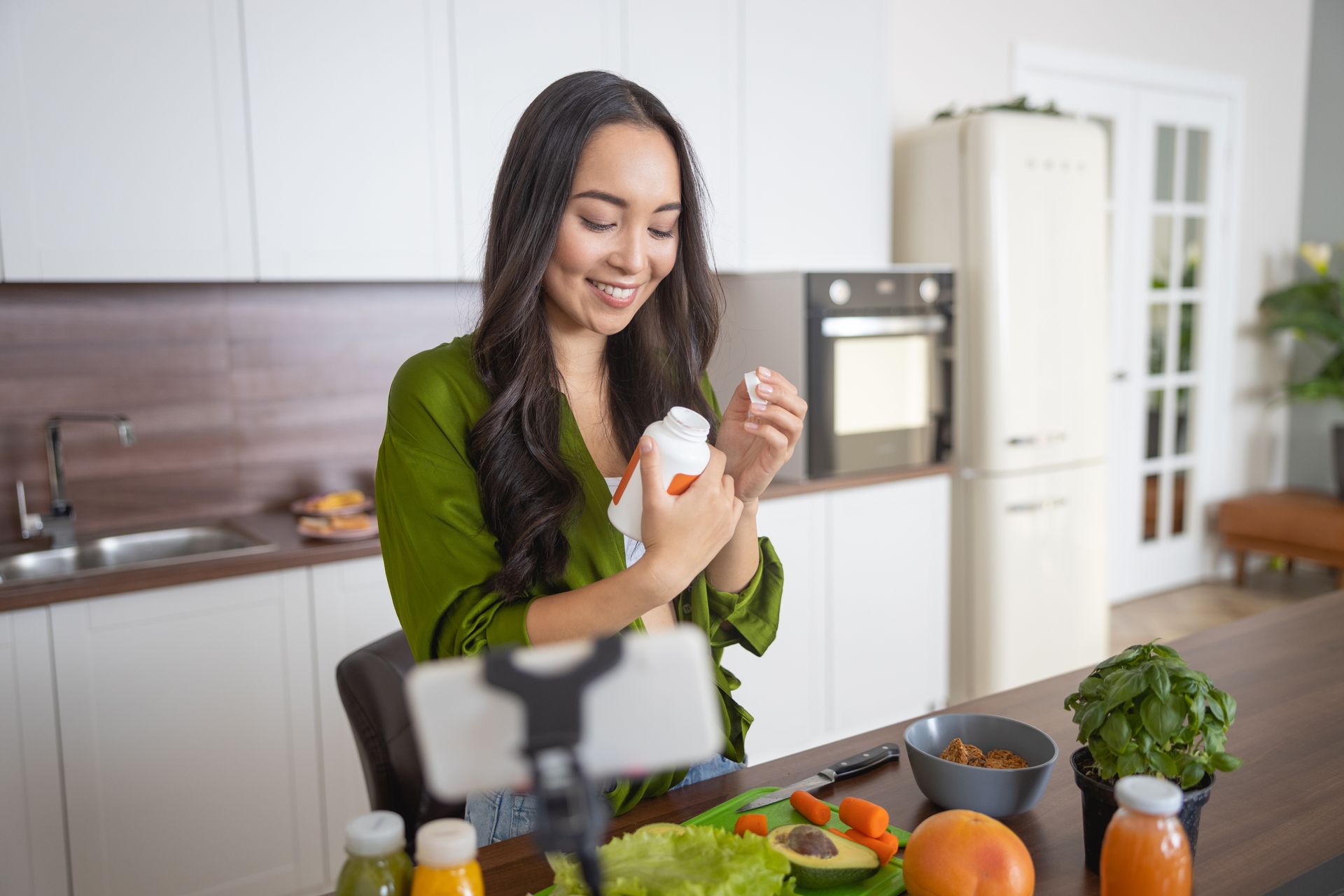 Woman preparing food in a bright kitchen, smiling beside fresh vegetables and a tablet on the counter