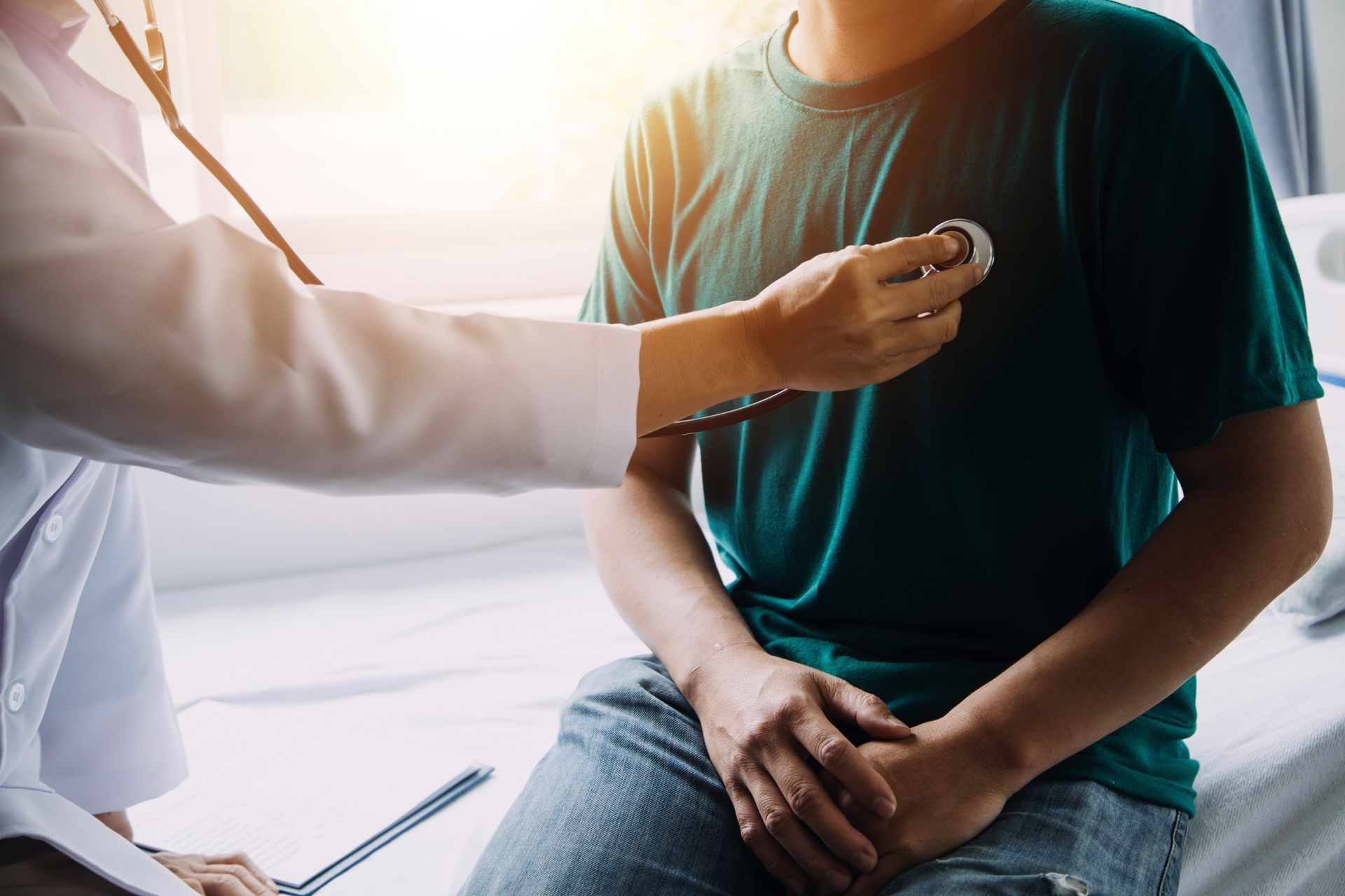 Doctor using a stethoscope to examine a seated patient in a green shirt