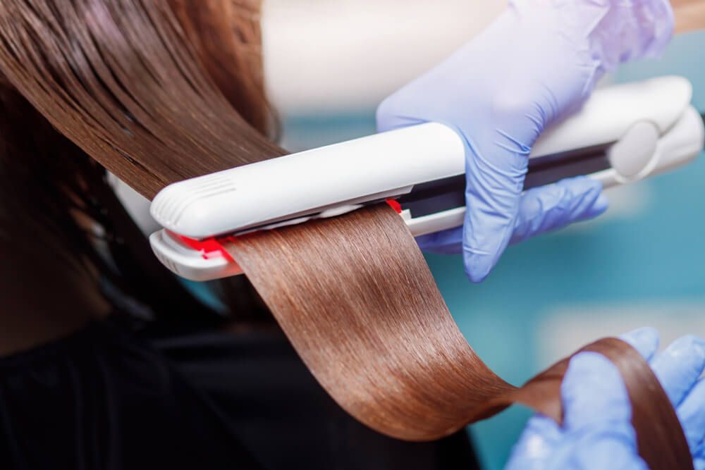 Hairstylist straightening a woman's hair — Hair It Is In Balgownie, NSW