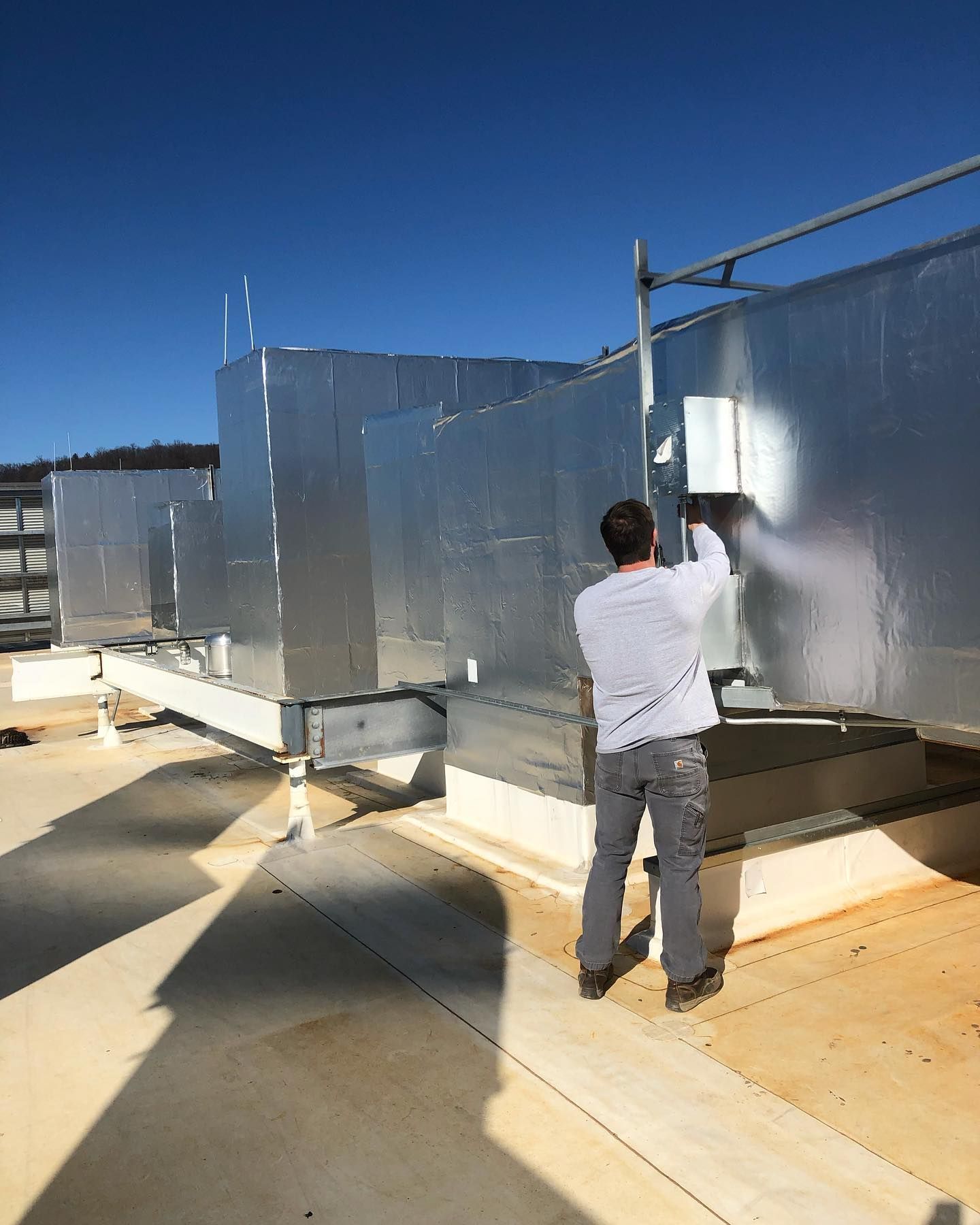 A man is standing on top of a roof working on a metal structure.