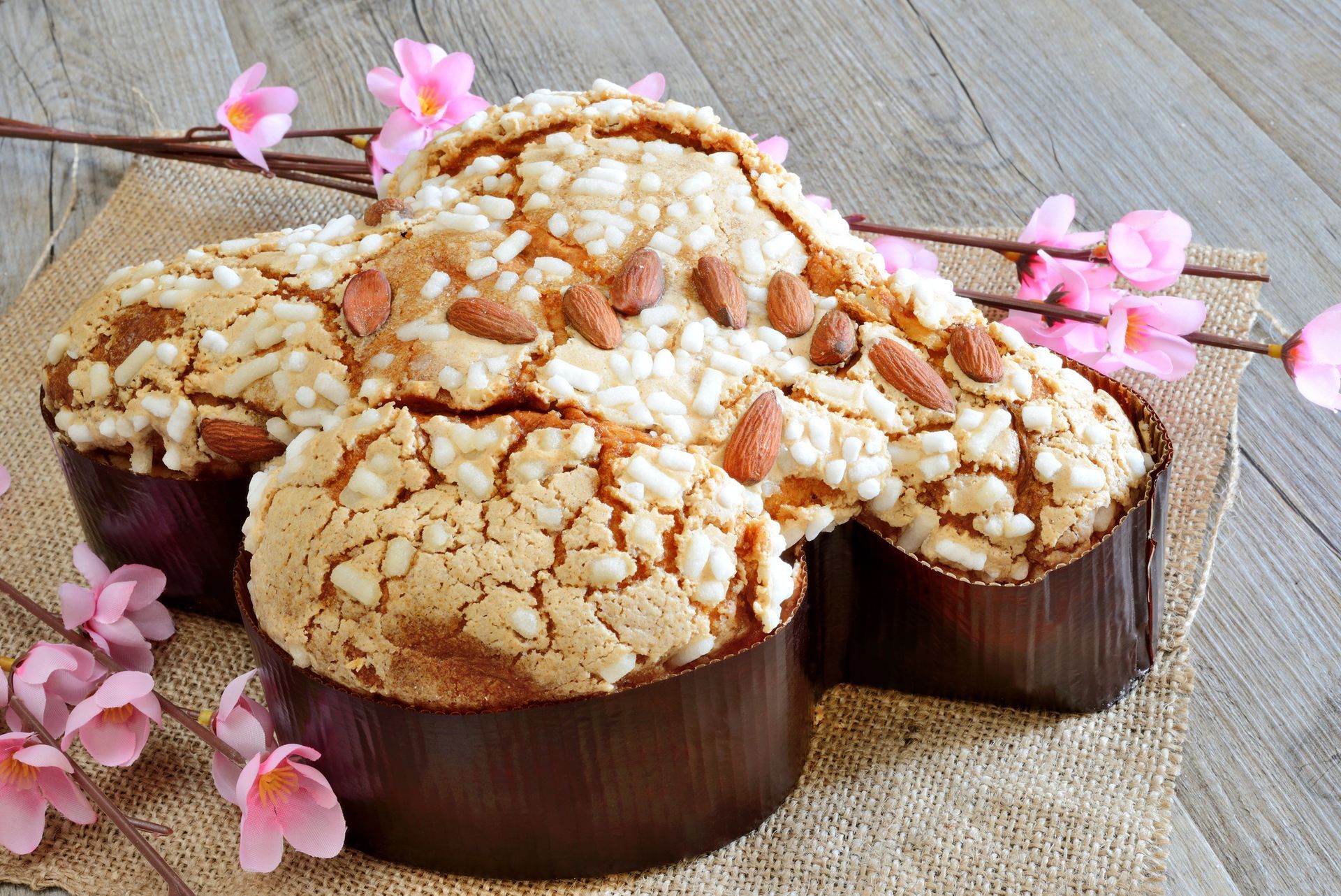 Tre pani con crosta di zucchero in stampi rotondi, decorati con fiori rosa su una superficie rustica