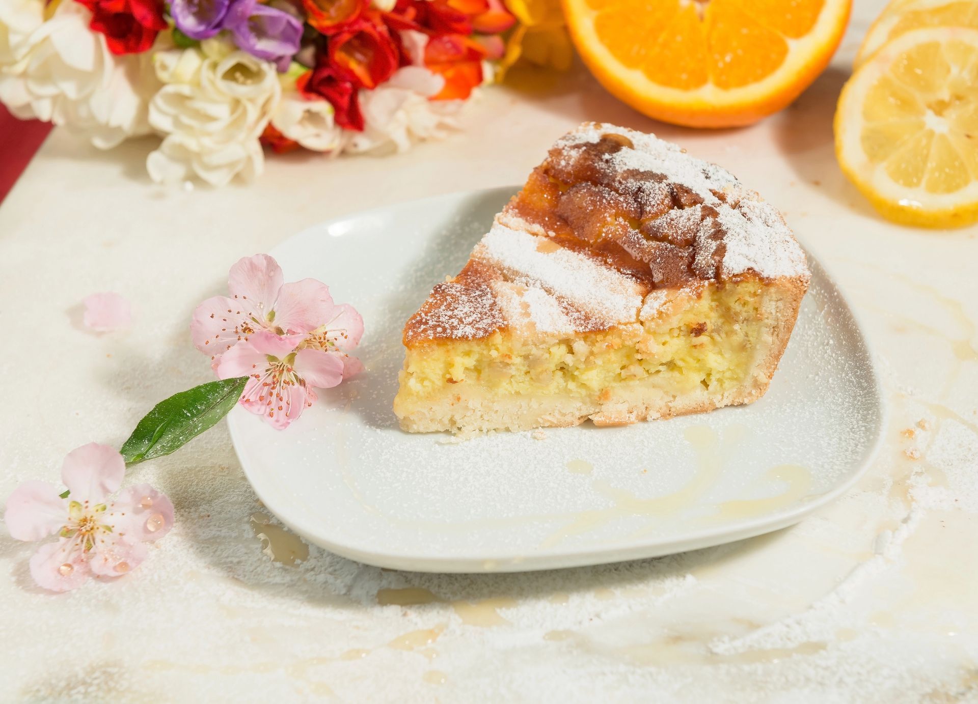 Fetta di torta con zucchero a velo su un piatto bianco, decorata con fette di limone e fiori.