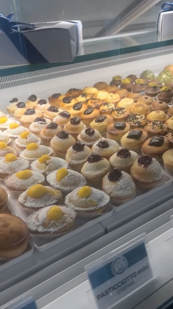 Vetrina da pasticceria piena di ciambelle assortite ricoperte di zucchero a velo e pasticcini con glassa al cioccolato e al limone.