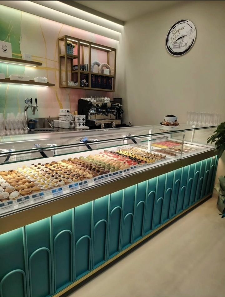 Vetrina da forno con un assortimento di pasticcini e torte in un luminoso interno di caffetteria.