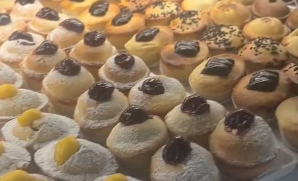 Vassoio di bignè assortiti glassati con guarnizioni al cioccolato e gialle, esposti in una pasticceria.