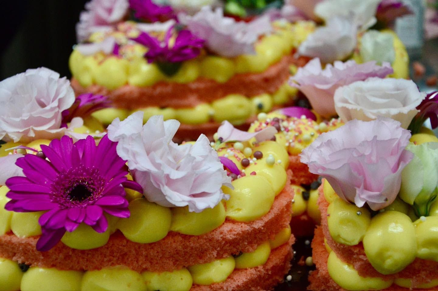 Torte decorate con fiori rosa e bianchi e glassa gialla, in una ripresa ravvicinata.