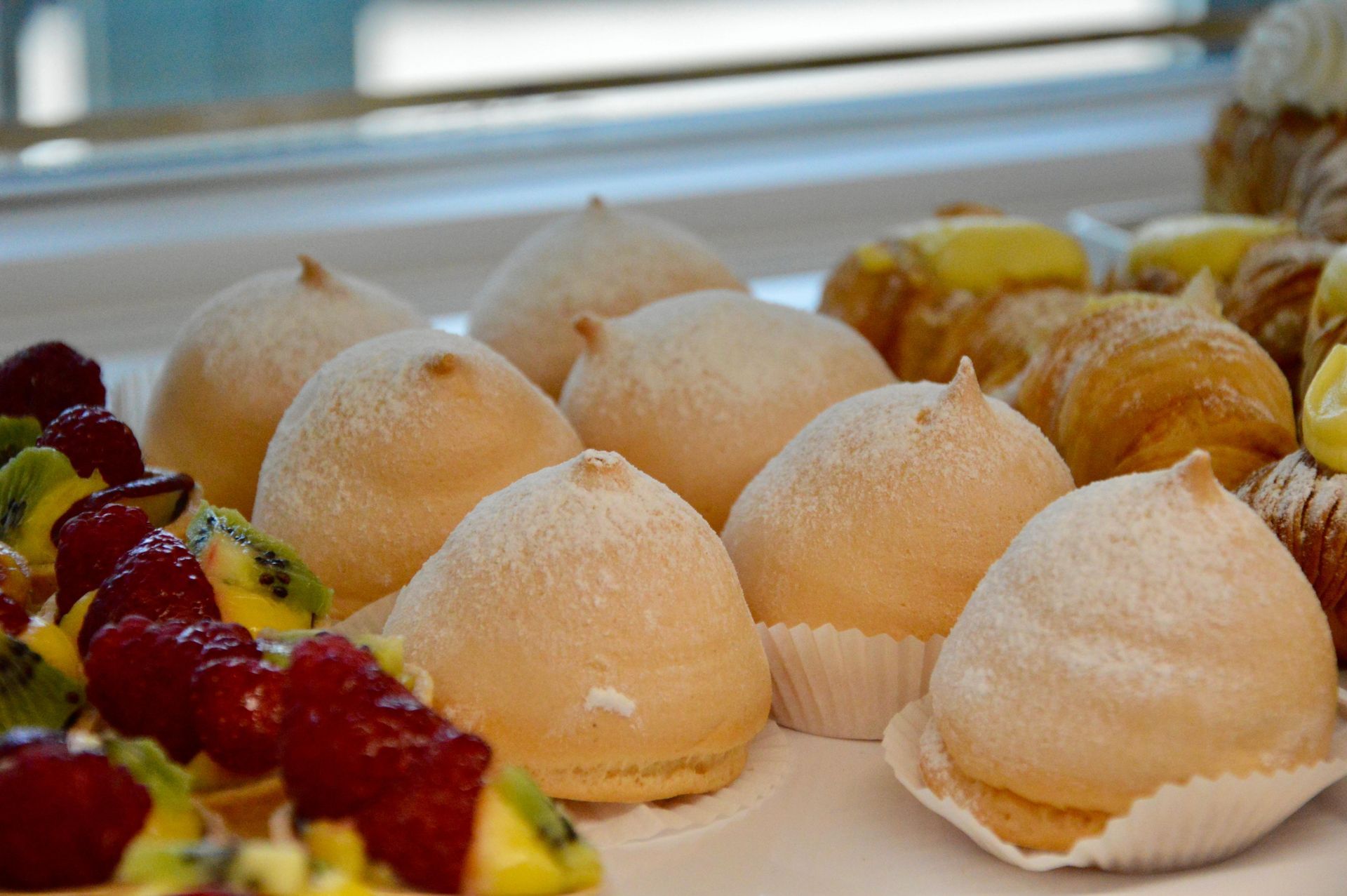 Un assortimento di pasticcini ripieni di crema, spolverati di zucchero a velo e disposti su un vassoio da dessert.