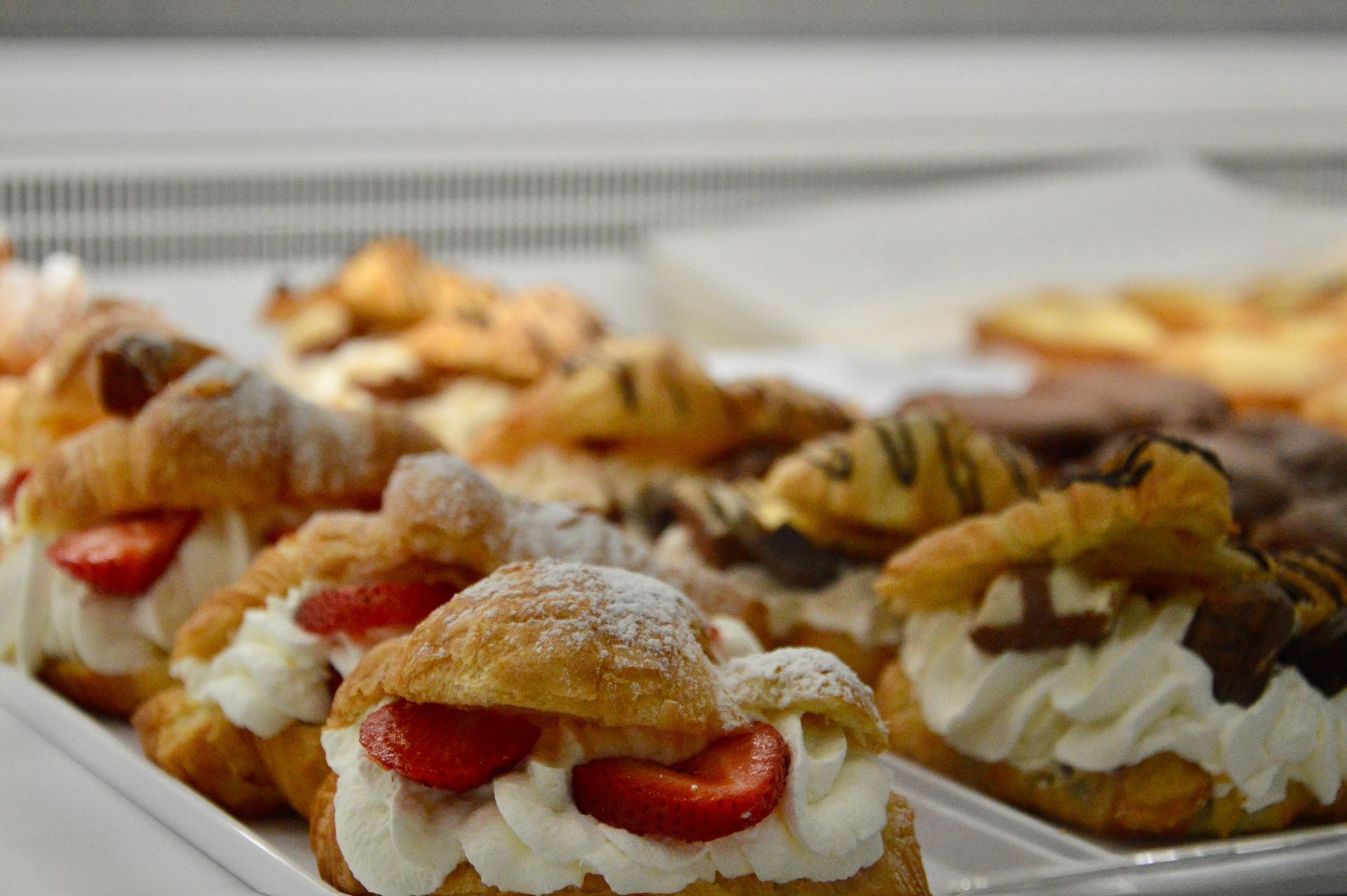 Un assortimento di pasticcini ripieni di crema con guarnizione di frutta su un vassoio al bancone di una pasticceria.