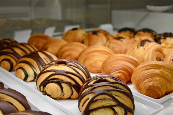 Vassoio di croissant assortiti, semplici e ricoperti di cioccolato, su un espositore da pasticceria.