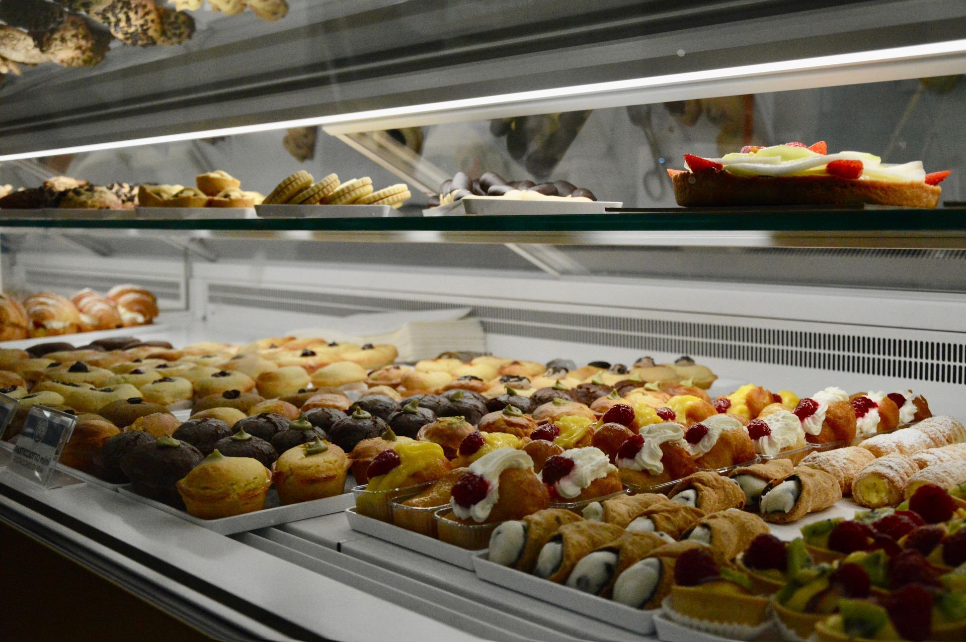 Vetrina di una pasticceria con un assortimento di pasticcini, muffin e crostate su vassoi.