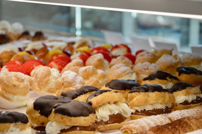 Pasticcini assortiti guarniti con cioccolato e frutta su vassoi da pasticceria.