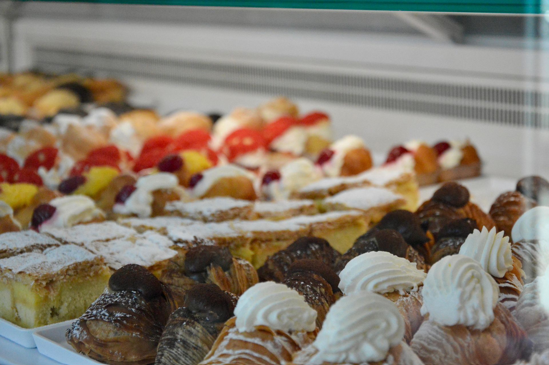 Un assortimento di pasticcini e crostate esposti in una vetrina, guarniti con zucchero a velo e panna montata.