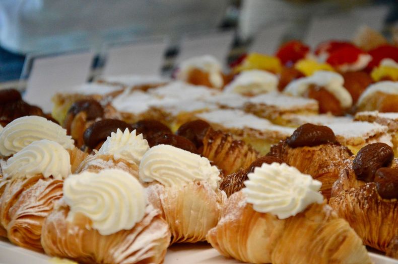 Pasticcini e croissant con panna e noci esposti in una vetrina di pasticceria.