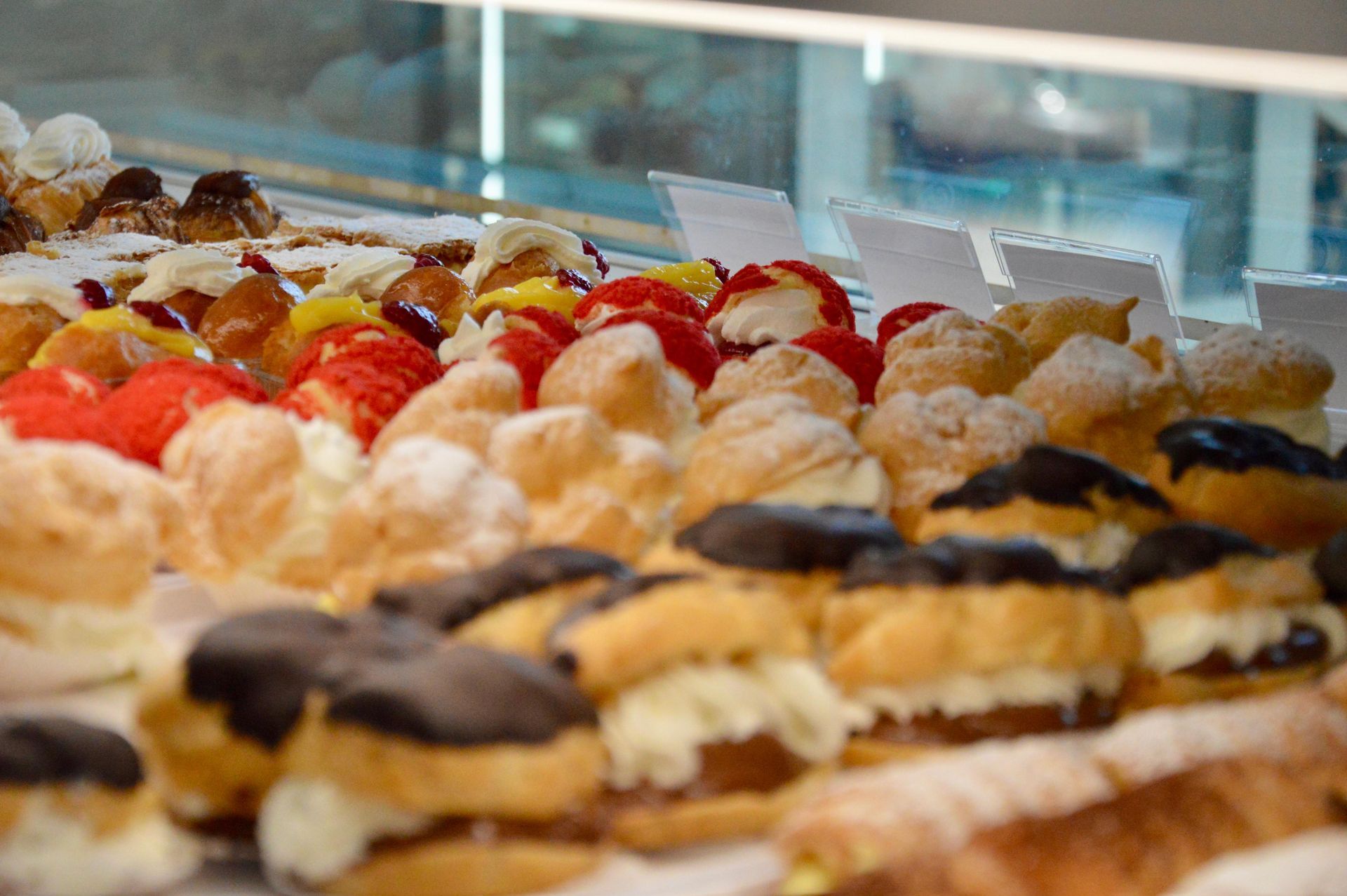 Assortimento di pasticcini glassati e dessert con frutta esposti in una vetrina da pasticceria.