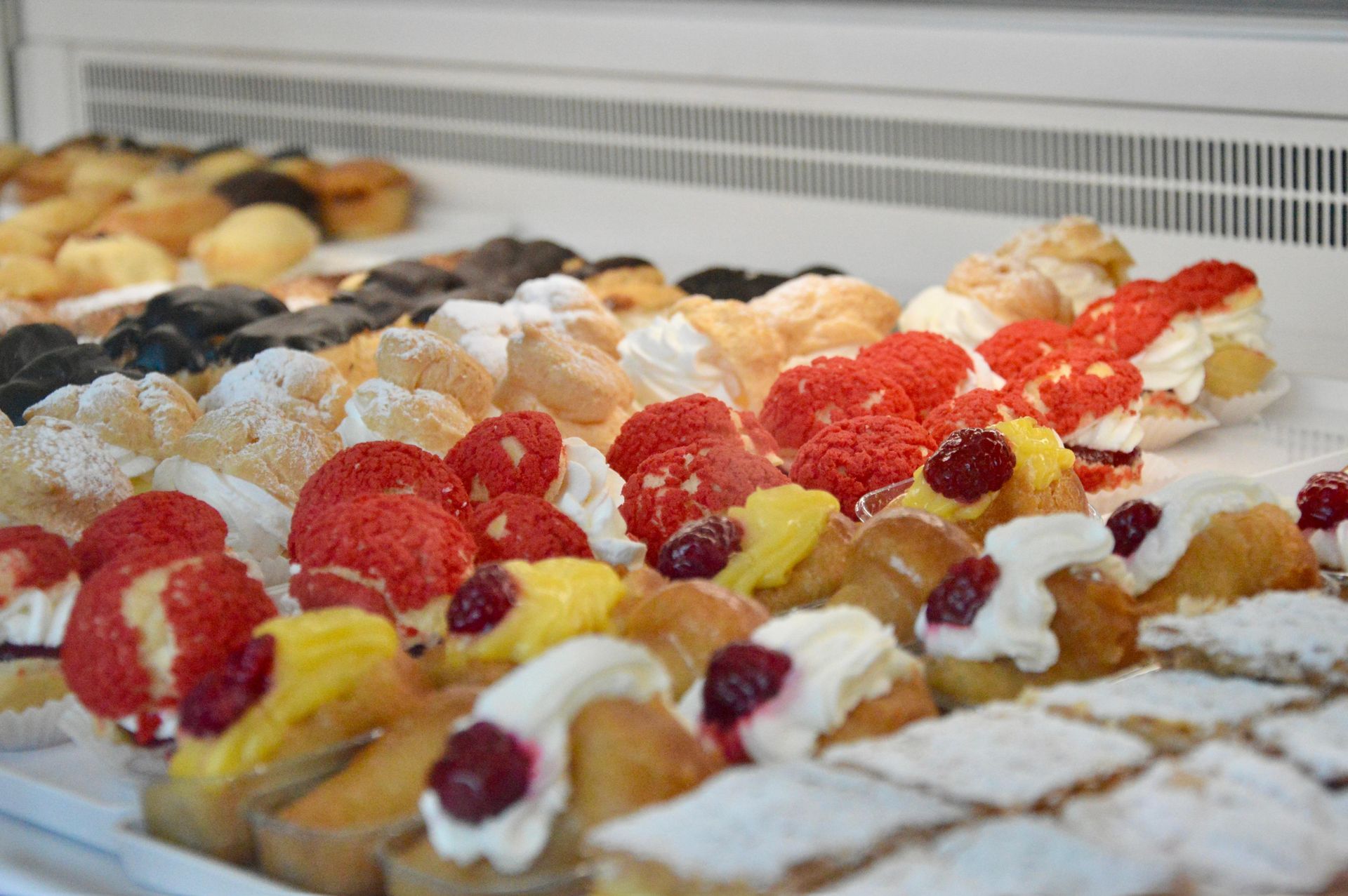 Vetrina di pasticceria con assortiti dessert guarniti con frutta, esposta in un banco frigo.