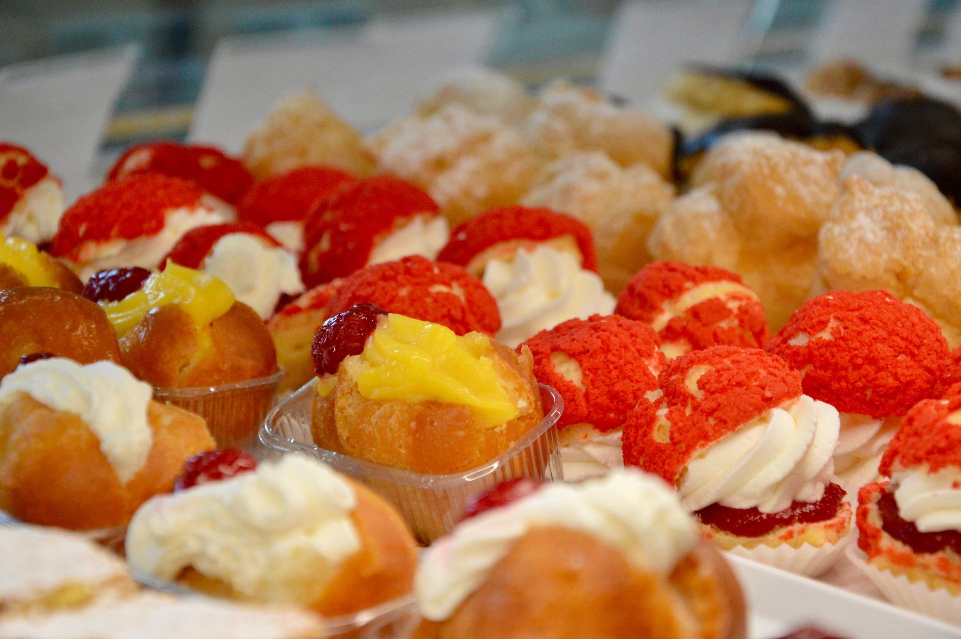 Assortimento di pasticcini ripieni di crema e guarniti con frutti rossi, disposti su un vassoio.