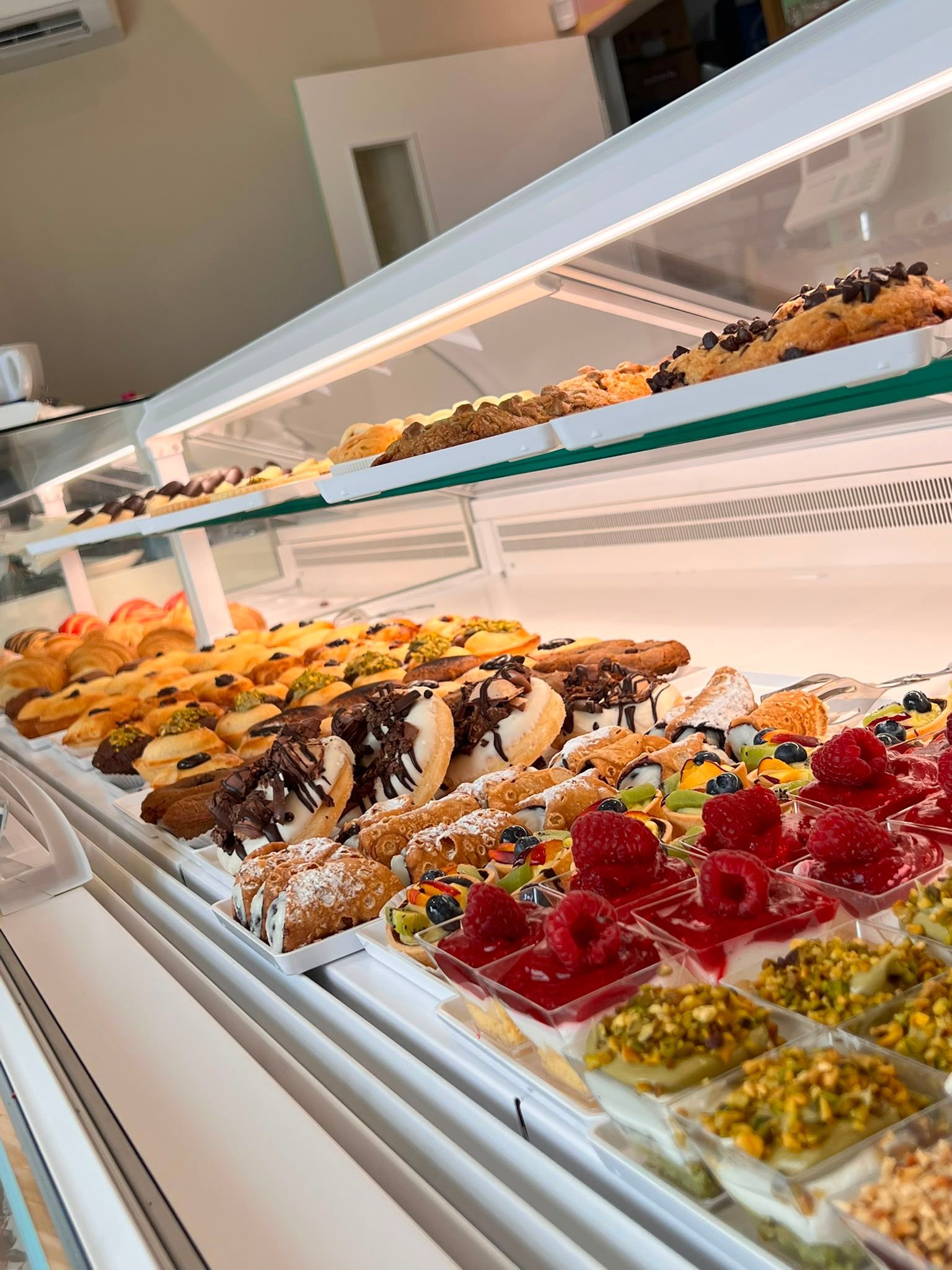 Un assortimento di pasticcini e dessert alla frutta esposti in una vetrina ben illuminata.
