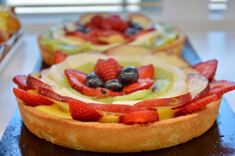 Una crostata di frutta con fragole e mirtilli su un tavolo, con altre crostate sfocate sullo sfondo.