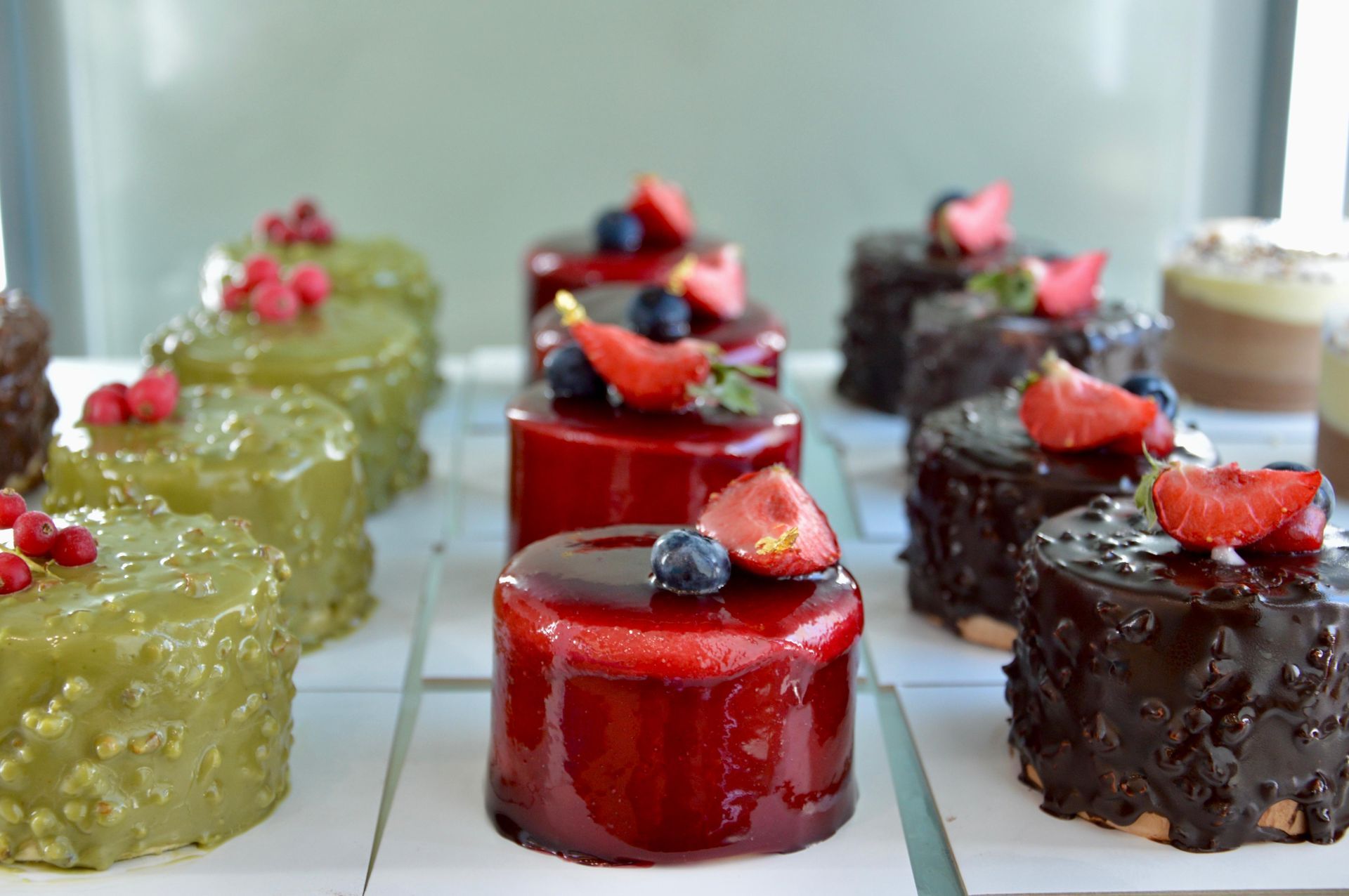 Assortimento di mini dessert lucidi a strati con frutti di bosco su un vassoio da esposizione.