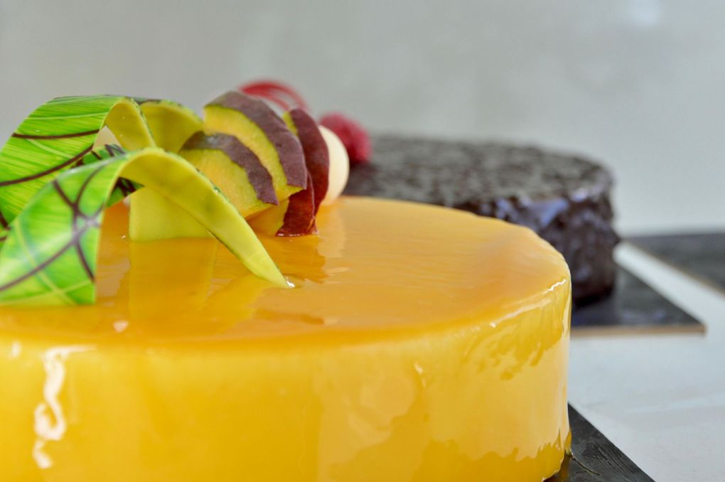 Torta glassata di giallo con guarnizione di frutta e un dessert al cioccolato sullo sfondo.