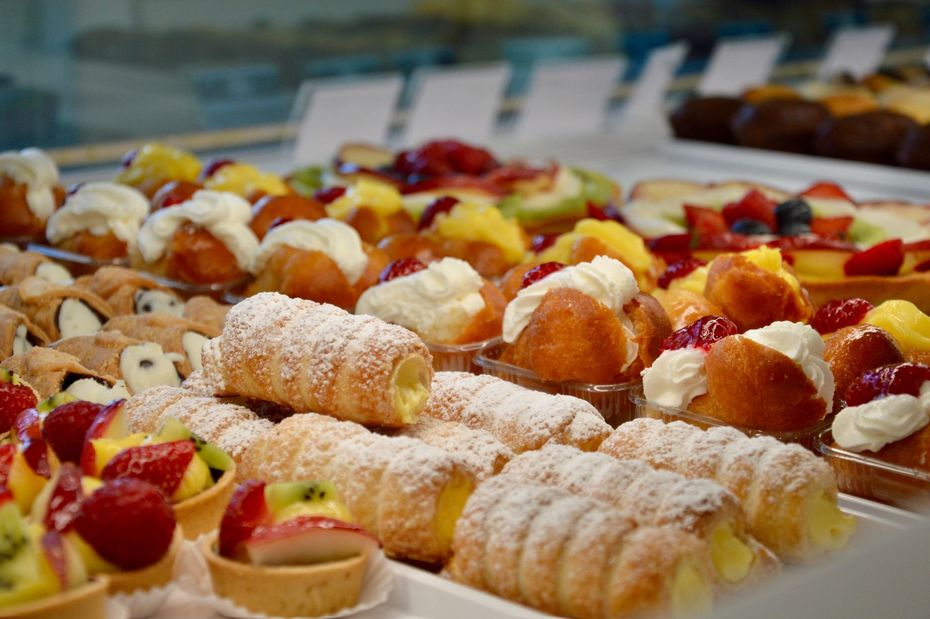 Assortimento di pasticcini e crostatine di frutta spolverati di zucchero a velo su un vassoio da esposizione di una pasticceria.