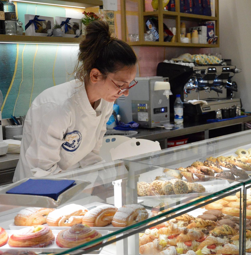 Un addetto di panetteria in uniforme bianca sistema i dolci dietro una vetrina.
