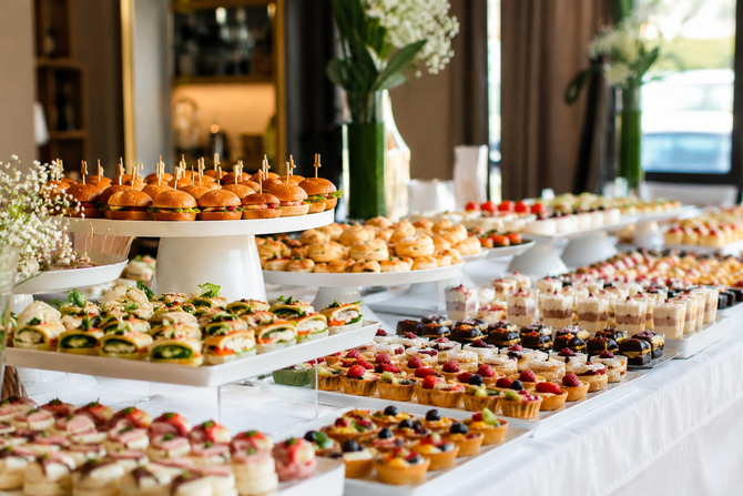 Un tavolo da buffet con file di dessert e pasticcini colorati in formato mignon disposti su alzatine bianche.