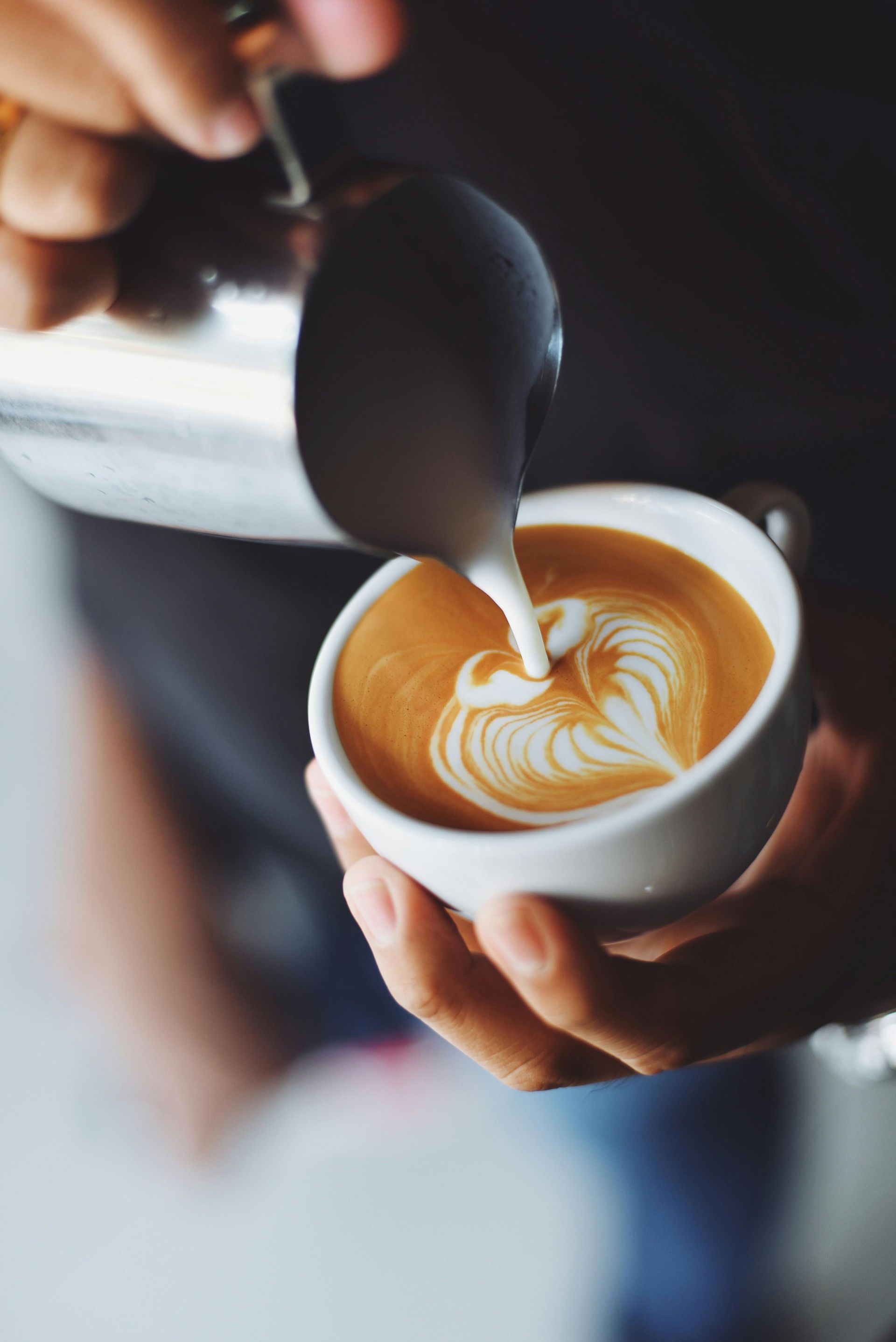 Barista pouring milk into coffee cup, creating heart-shaped latte art.