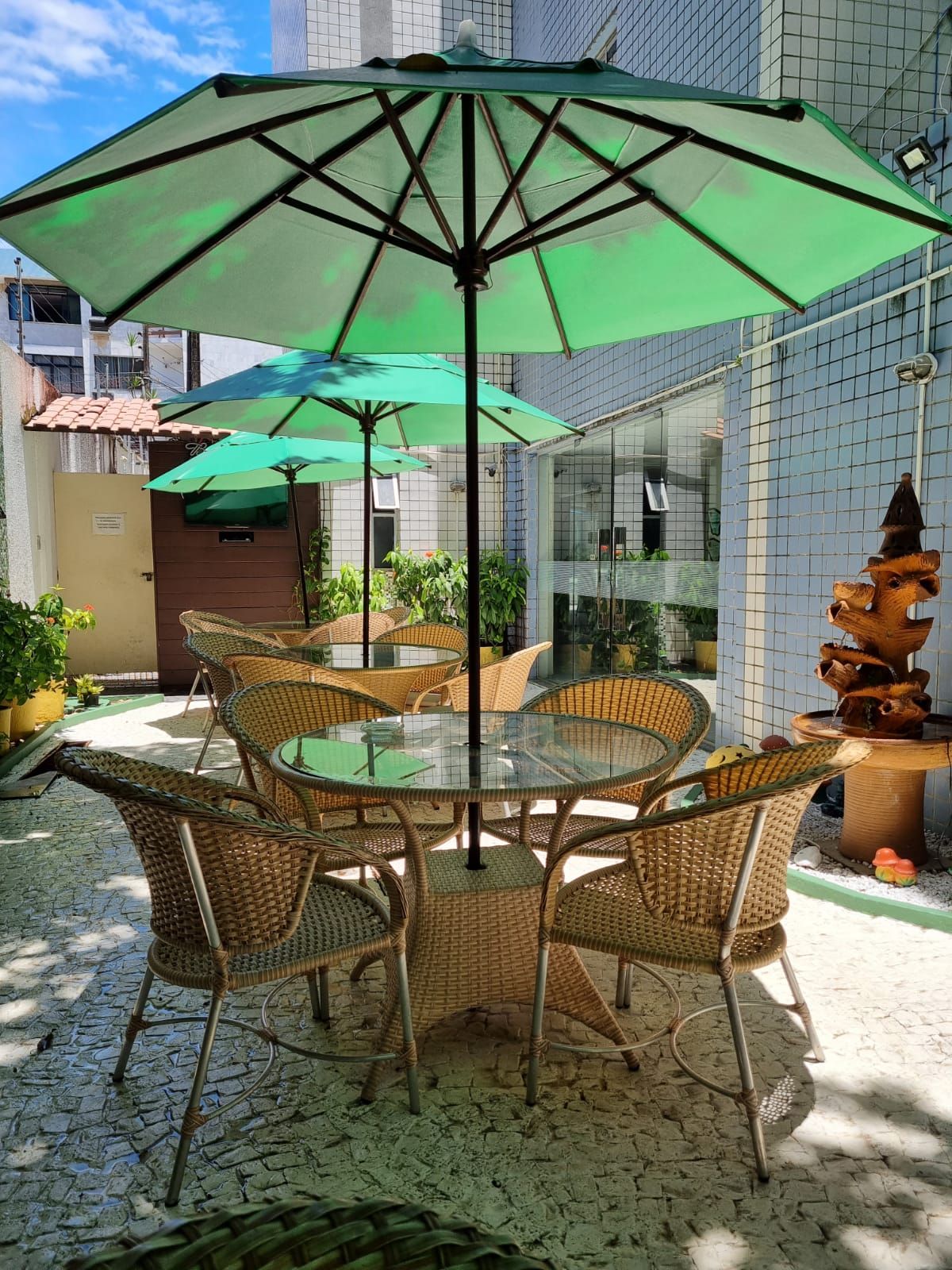 Um pátio com uma mesa e cadeiras sob guarda-sóis verdes. Vila Azul Praia Hotel