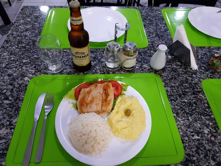 Um prato de comida e uma garrafa de cerveja em uma mesa Vila Azul Praia Hotel