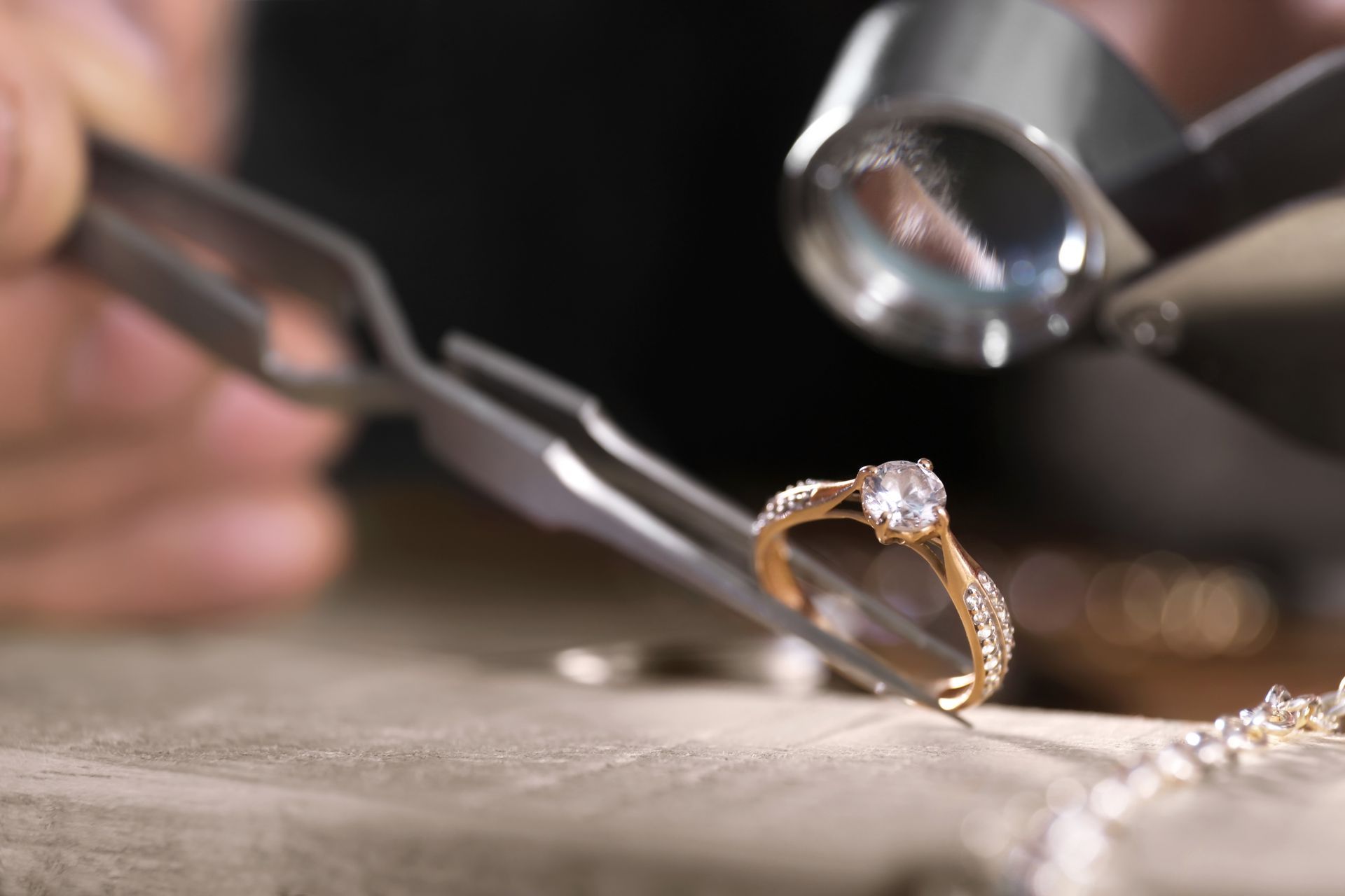 Close-up of a jeweler inspecting a diamond ring with tools on a workbench.