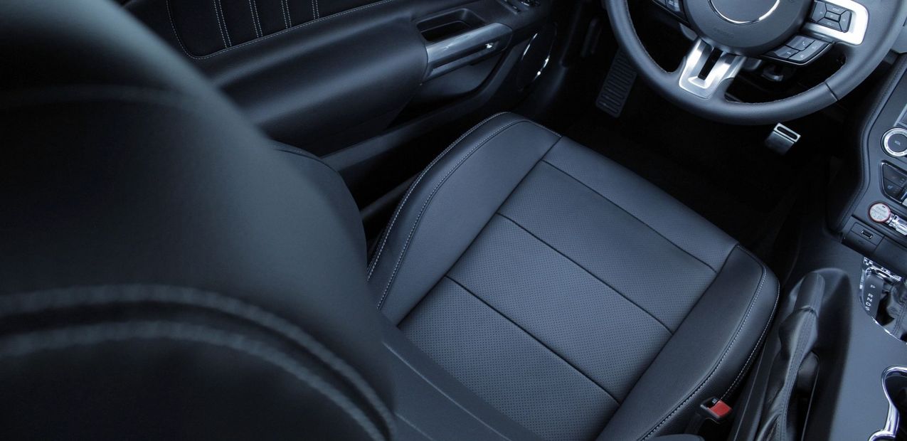 Interno di un veicolo che mostra il sedile del conducente in pelle nera con dettagli traforati e il volante.