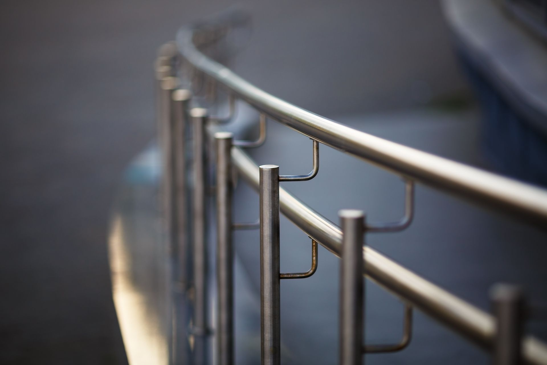 Curved metal handrail beside steps, with blurred blue-gray background and warm light reflection