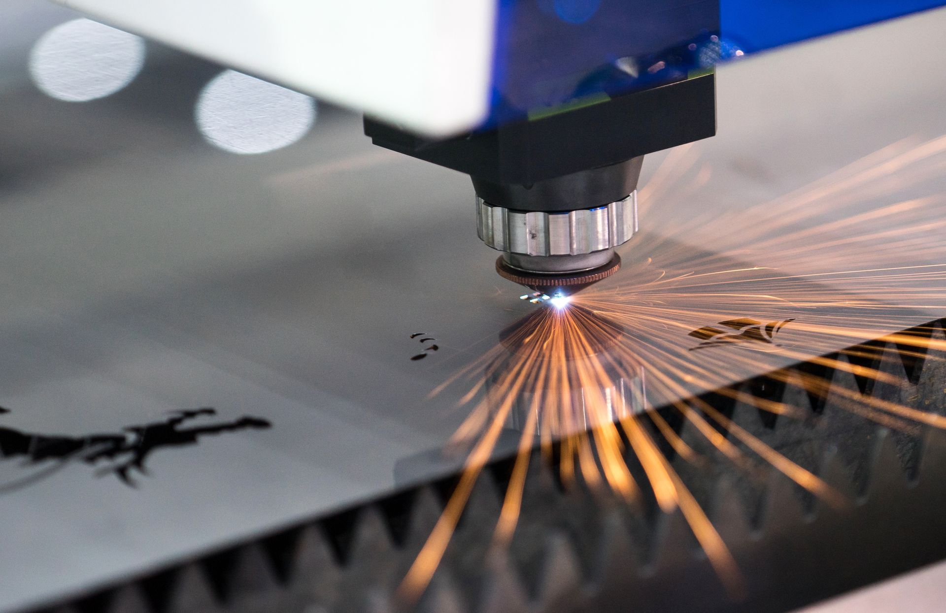 Laser cutter cutting metal sheet with bright orange sparks flying across the surface