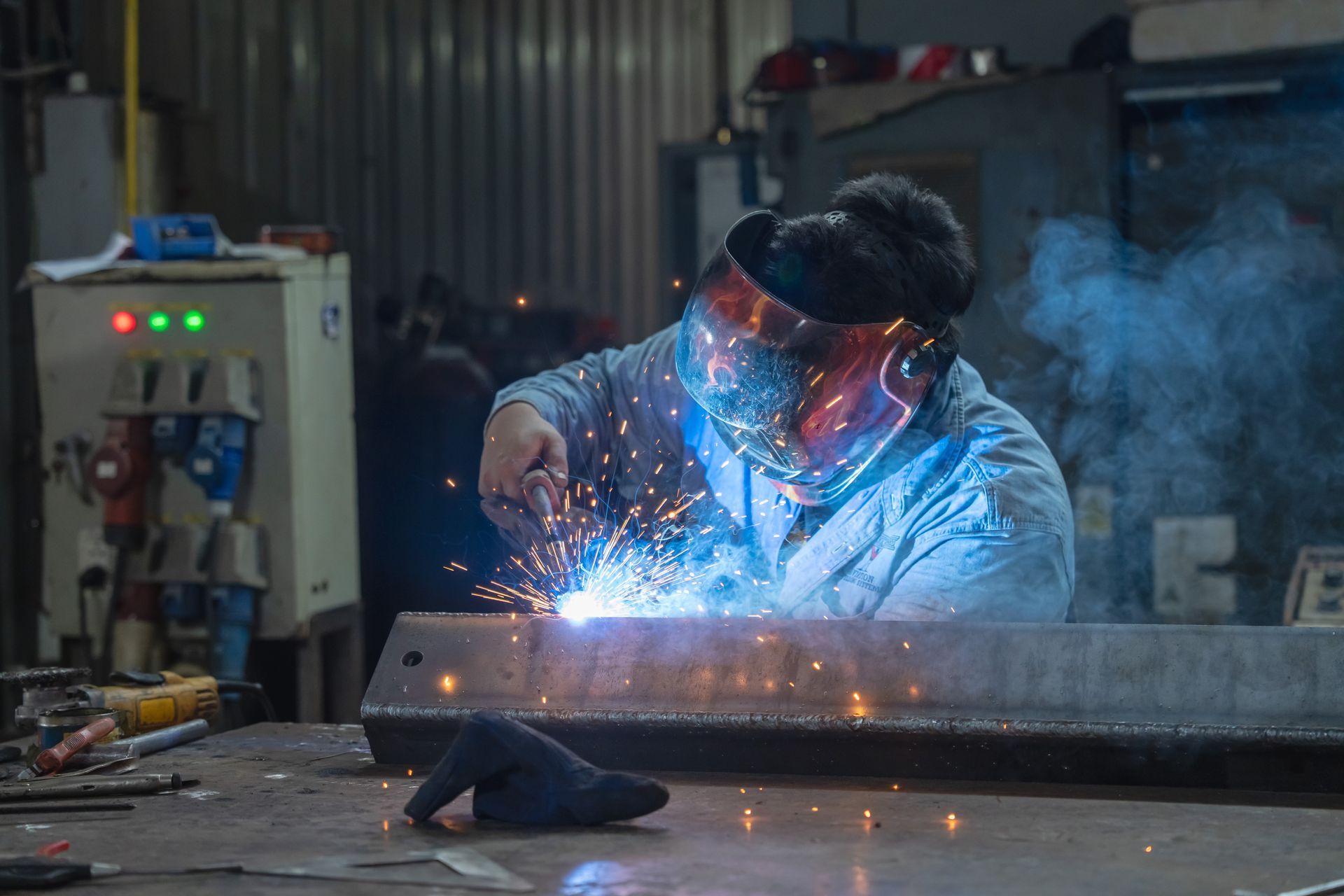 Worker welding metal in a workshop, with bright blue sparks and smoke.