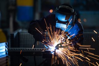 Welder in blue protective gear sparks metal in a dim workshop