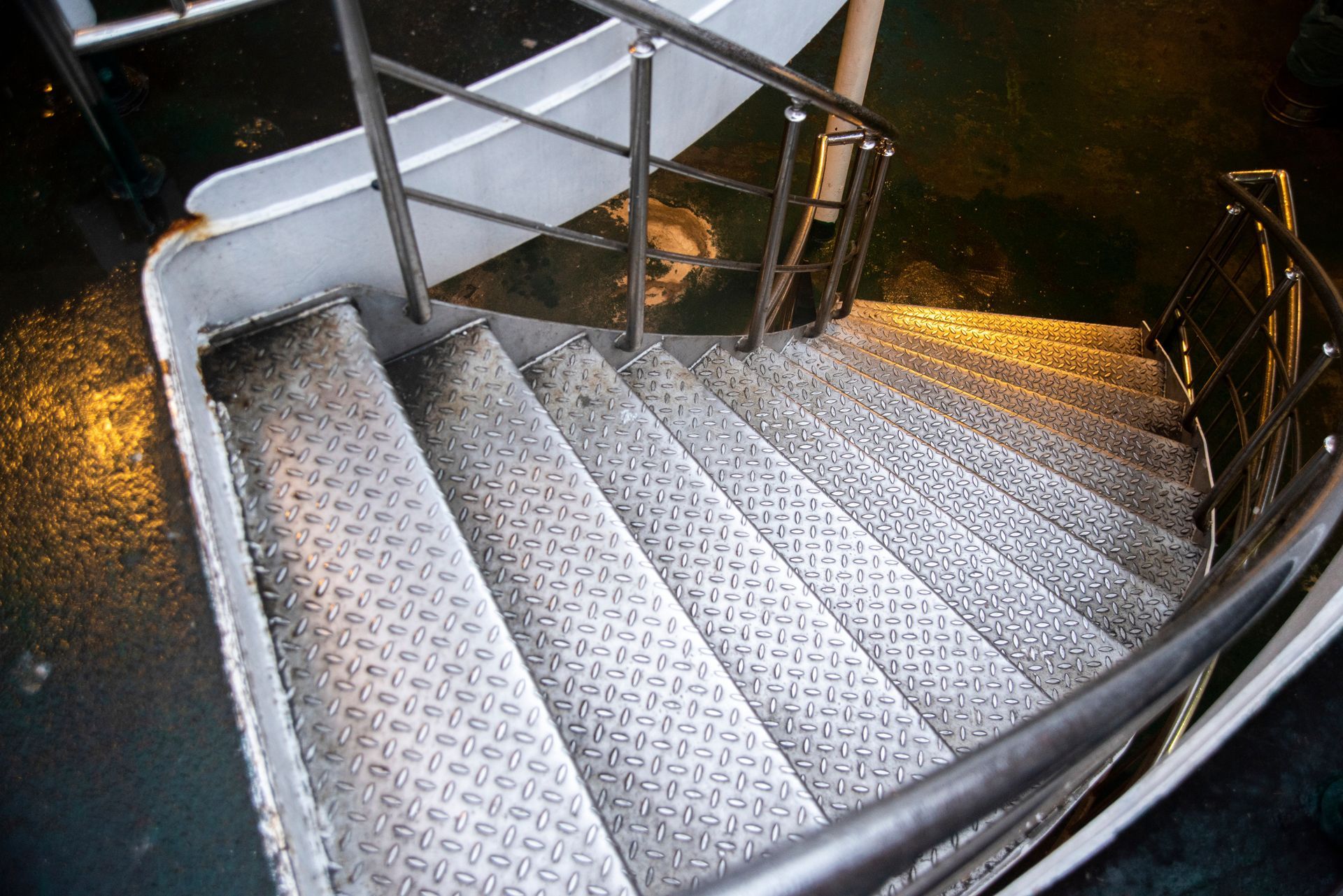 Metal spiral staircase with grated steps and railings in a dimly lit industrial setting
