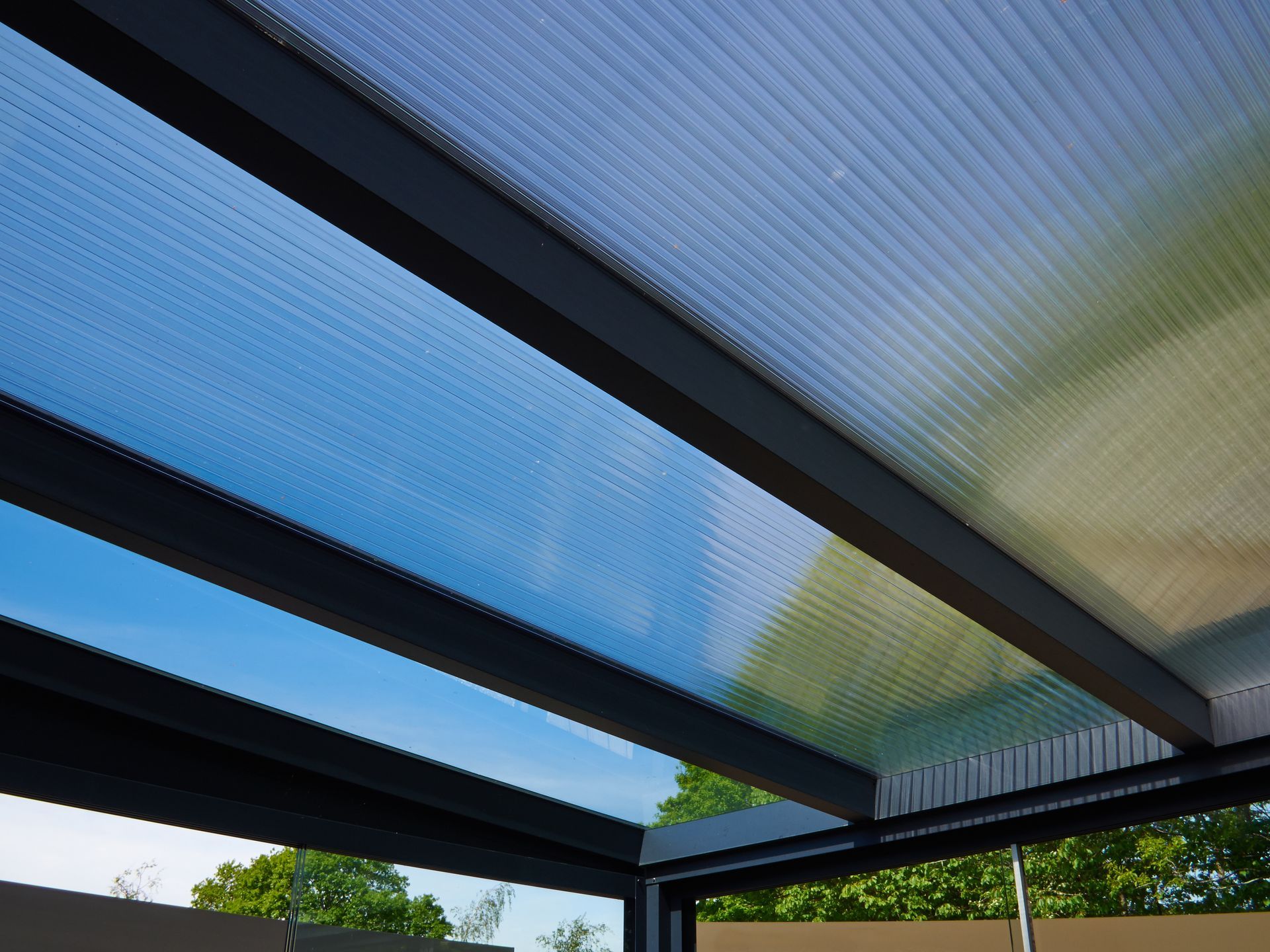 Blue-tinted translucent roof panels with dark beams above a garden view