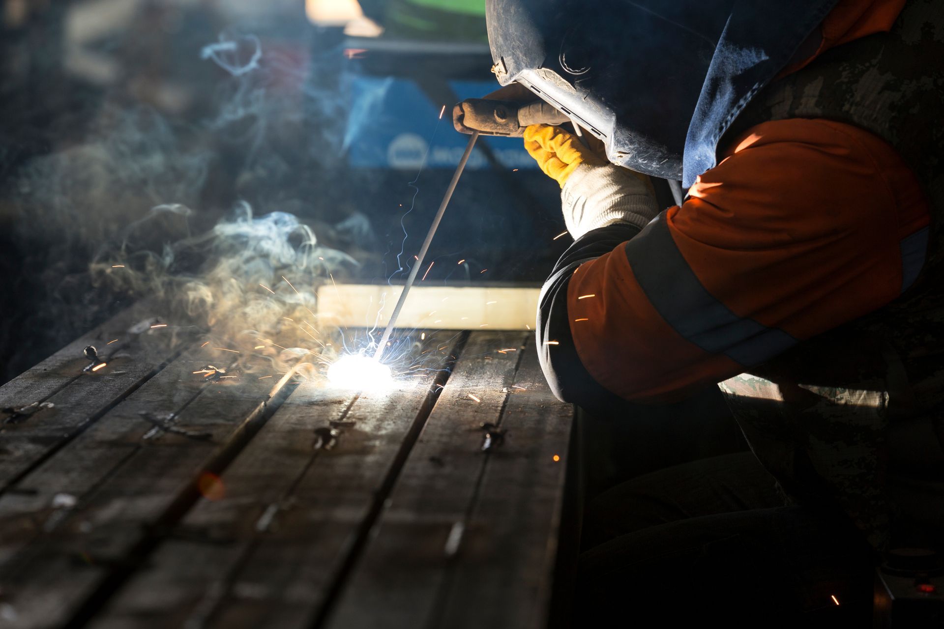 Worker welding on a metal surface, bright sparks and smoke in a dim workshop