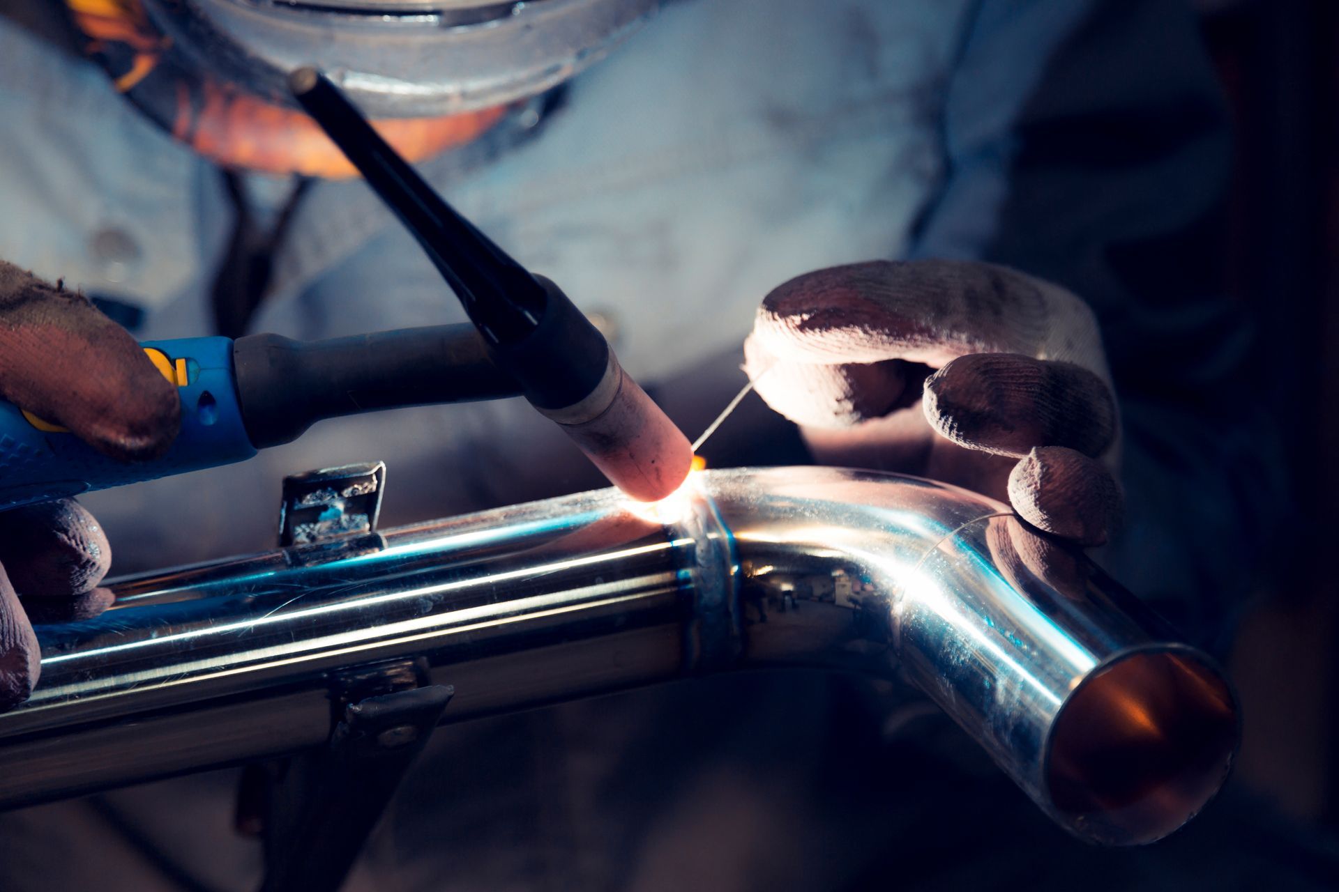 Person welding a shiny metal pipe with a torch in a workshop