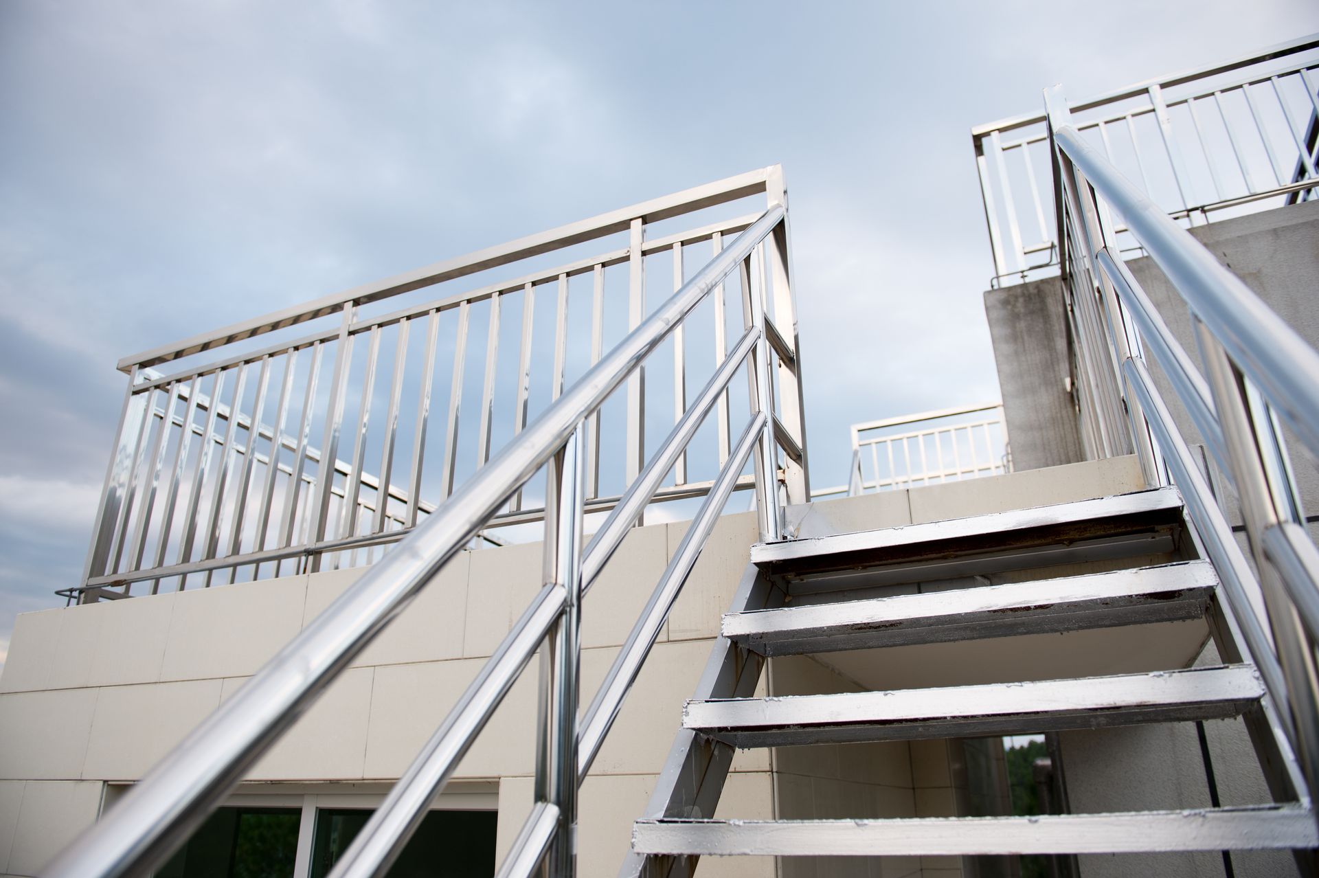 Stairway with metal railings leading up to a rooftop against a cloudy sky